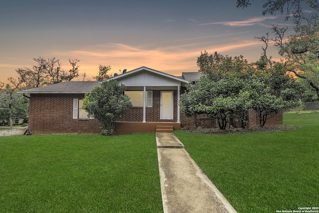 view of front of home featuring a yard, covered porch, brick siding, and a shingled roof