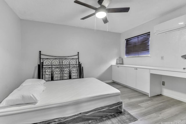 bedroom featuring light wood-style flooring, a wall unit AC, baseboards, ceiling fan, and built in study area