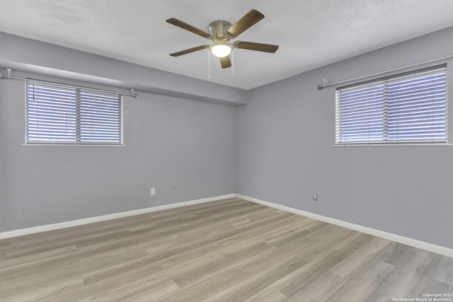 empty room with ceiling fan, wood finished floors, baseboards, and a textured ceiling