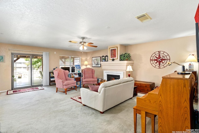 carpeted living room with visible vents, a lit fireplace, a ceiling fan, and a textured ceiling