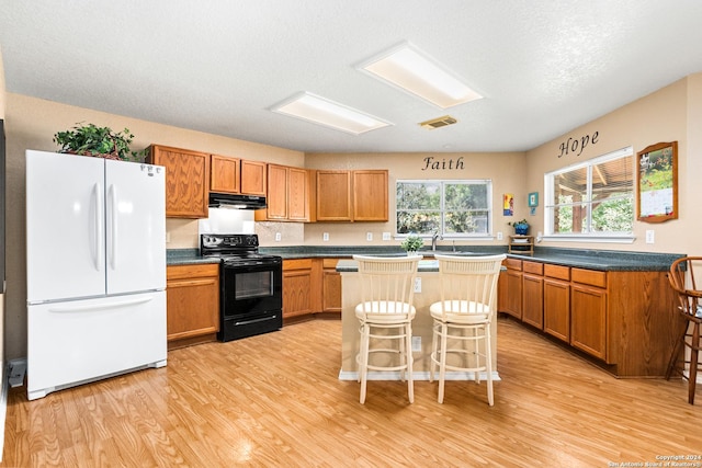 kitchen with under cabinet range hood, black / electric stove, light wood-style flooring, and freestanding refrigerator