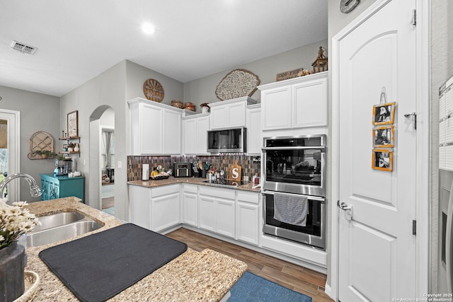 kitchen featuring decorative backsplash, white cabinets, stainless steel appliances, and a sink