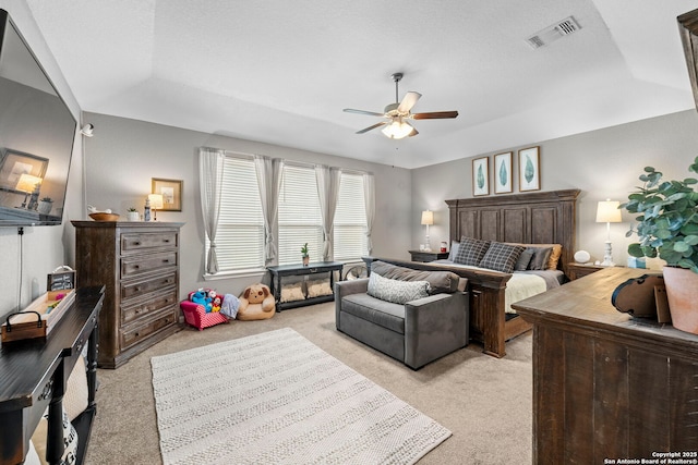 bedroom with a tray ceiling, visible vents, light carpet, and a ceiling fan