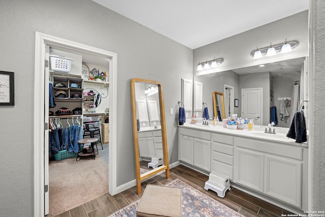 full bath featuring double vanity, a spacious closet, wood finish floors, and a sink