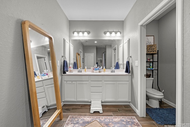 bathroom with a sink, double vanity, toilet, and wood tiled floor