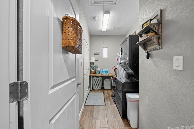 interior space with wood finish floors, a textured ceiling, attic access, and a textured wall