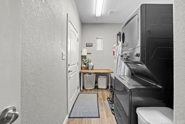 laundry area featuring wood finish floors, visible vents, stacked washer / dryer, laundry area, and a textured wall