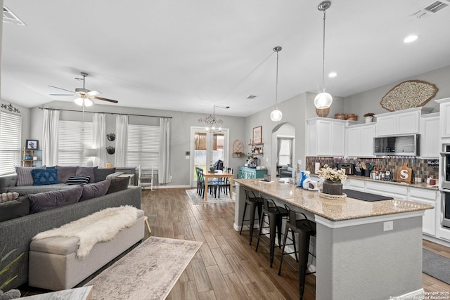 kitchen featuring backsplash, open floor plan, a kitchen breakfast bar, wood finished floors, and stainless steel appliances