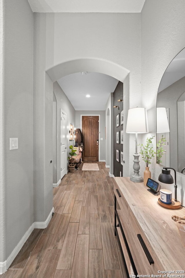 corridor with wood finished floors, arched walkways, and baseboards