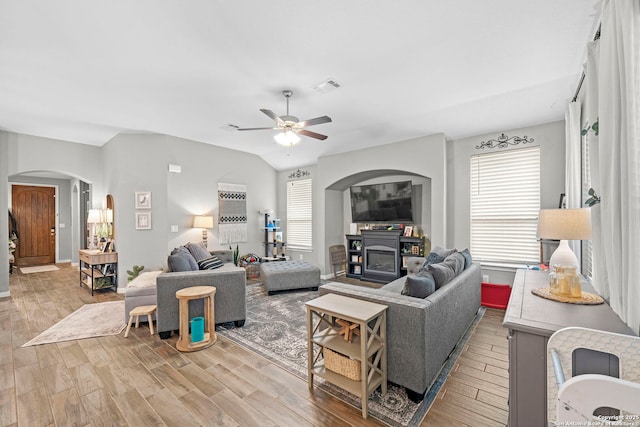 living area featuring wood finished floors, visible vents, lofted ceiling, arched walkways, and a glass covered fireplace