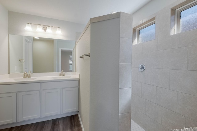 bathroom featuring a sink, wood finished floors, double vanity, and a tile shower