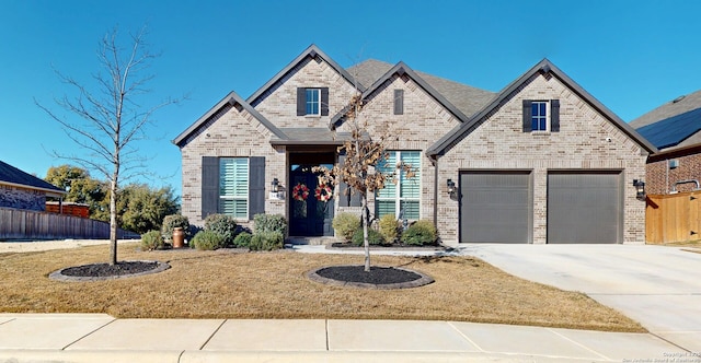 french country style house with brick siding, concrete driveway, a front lawn, and fence