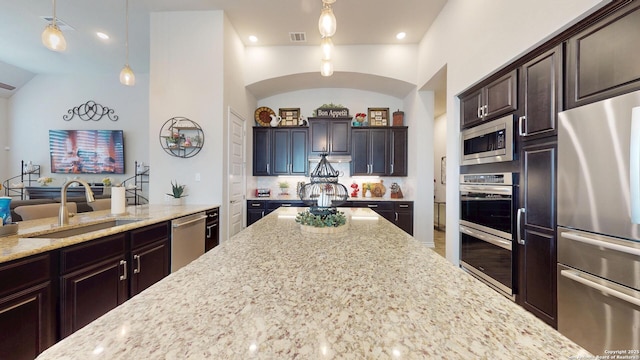 kitchen featuring visible vents, light stone countertops, dark brown cabinetry, appliances with stainless steel finishes, and a sink