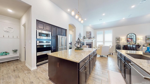 kitchen with light stone countertops, a fireplace, arched walkways, a sink, and appliances with stainless steel finishes