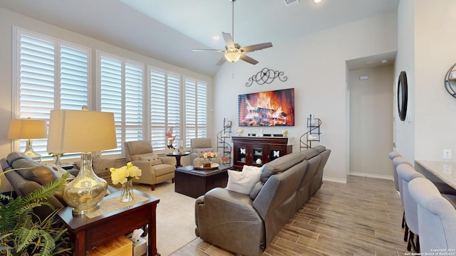 living area with a ceiling fan, baseboards, light wood finished floors, visible vents, and vaulted ceiling