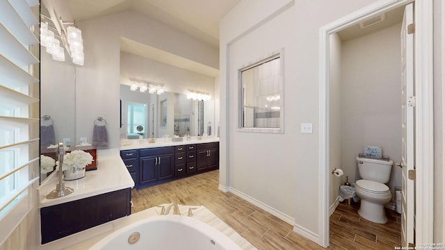 bathroom with wood tiled floor, toilet, a bath, vanity, and vaulted ceiling