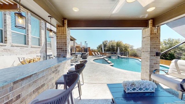 view of pool featuring outdoor dry bar, a pool with connected hot tub, fence, a ceiling fan, and a patio