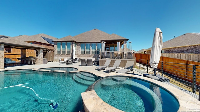 view of pool with a patio area, fence, a pool with connected hot tub, and outdoor dry bar