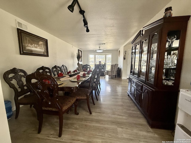 dining space featuring visible vents, rail lighting, a textured ceiling, and light wood-style floors