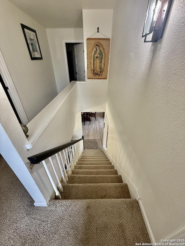 stairway with carpet and a textured wall