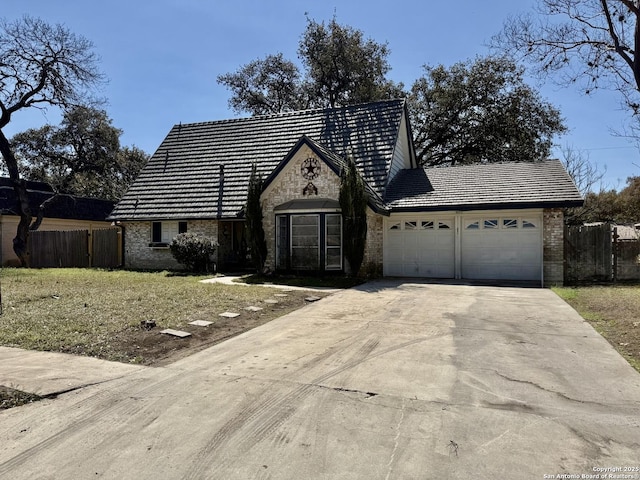 view of front facade with an attached garage, fence, brick siding, and driveway