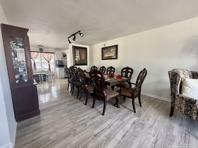 dining space featuring rail lighting, wood finished floors, baseboards, and a textured ceiling