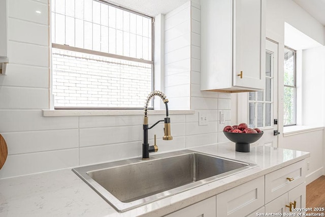 kitchen with wood finished floors, light stone countertops, a sink, decorative backsplash, and white cabinets