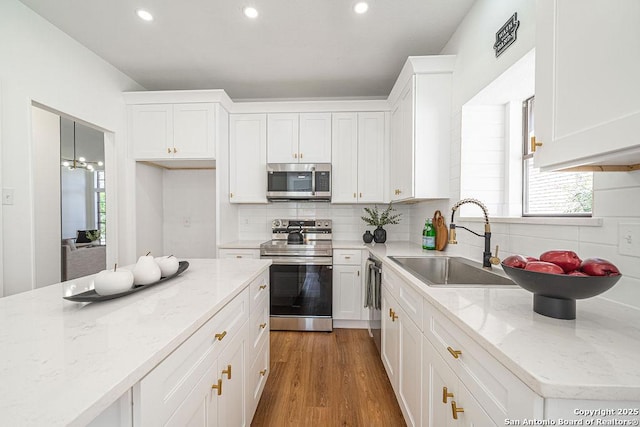 kitchen featuring decorative backsplash, appliances with stainless steel finishes, wood finished floors, white cabinetry, and a sink