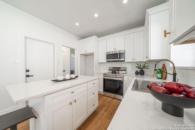 kitchen featuring light stone counters, a sink, appliances with stainless steel finishes, white cabinetry, and backsplash