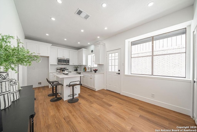 kitchen with light wood finished floors, backsplash, a breakfast bar area, appliances with stainless steel finishes, and white cabinets