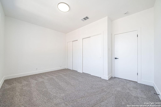 unfurnished bedroom with visible vents, carpet floors, baseboards, and multiple closets