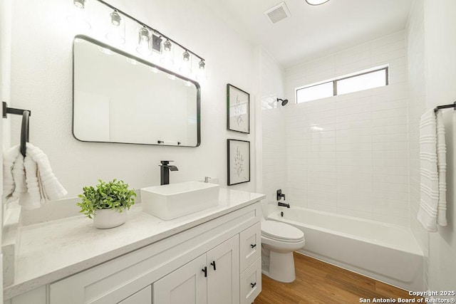 bathroom featuring visible vents, shower / washtub combination, toilet, wood finished floors, and vanity