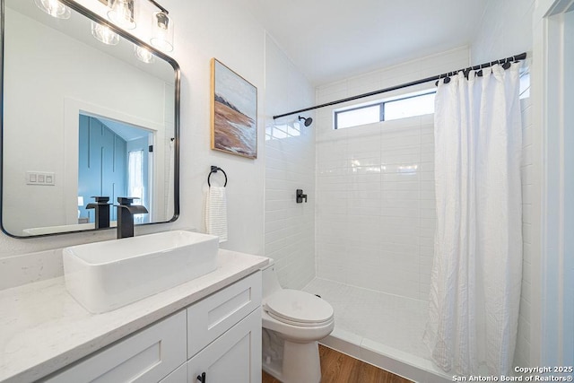 full bathroom with vanity, toilet, wood finished floors, and tiled shower