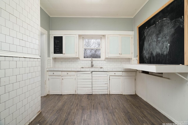 kitchen with dark wood-type flooring, a sink, white cabinets, crown molding, and glass insert cabinets