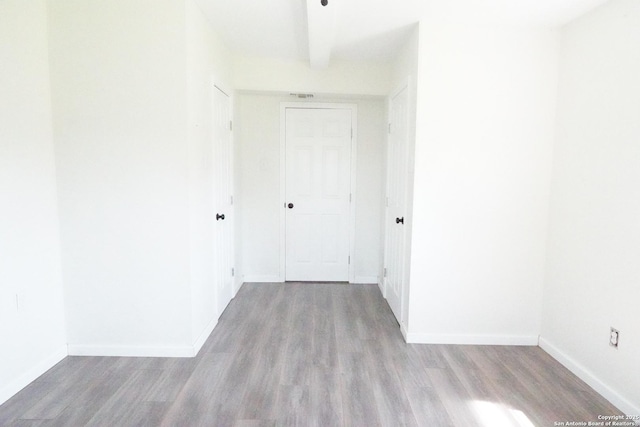 empty room with visible vents, beamed ceiling, wood finished floors, and baseboards