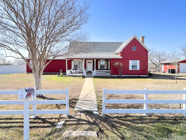 view of front of house featuring a fenced front yard, board and batten siding, covered porch, a front yard, and a chimney