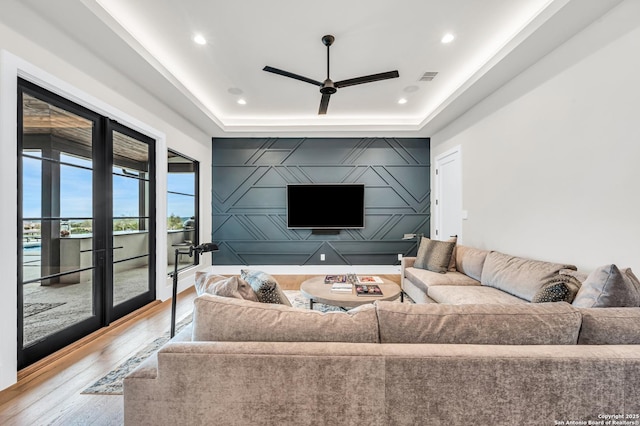 living area with an accent wall, a tray ceiling, wood finished floors, and visible vents