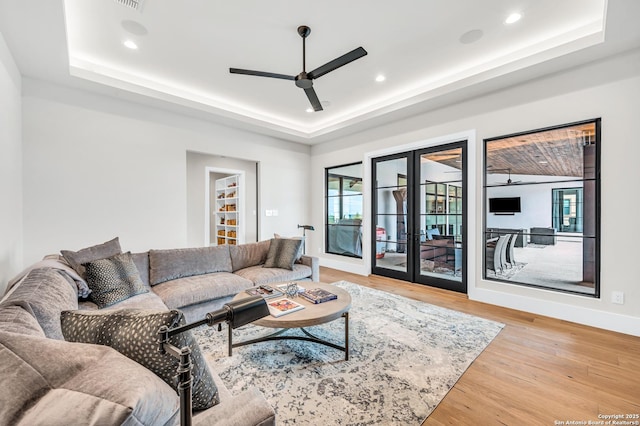 living area with a ceiling fan, wood finished floors, a tray ceiling, recessed lighting, and french doors