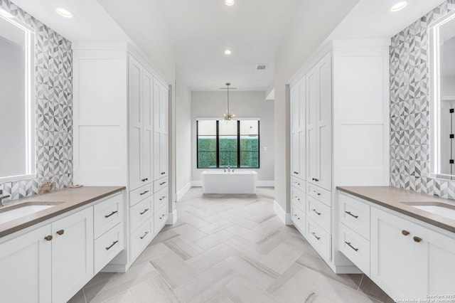 bathroom featuring a freestanding bath, two vanities, a closet, and a sink