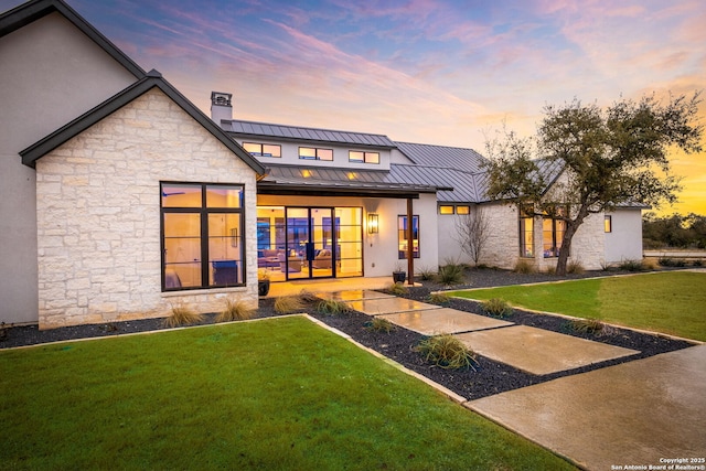 view of front of home featuring stucco siding, a standing seam roof, a front yard, metal roof, and a chimney