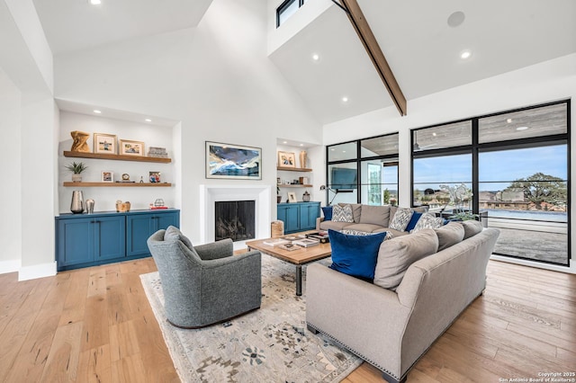 living area with light wood finished floors, built in features, a fireplace, and high vaulted ceiling