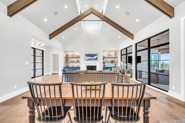 dining space with beam ceiling, a fireplace, light wood-style floors, and high vaulted ceiling