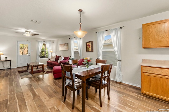 dining room featuring light wood finished floors, visible vents, a ceiling fan, and baseboards