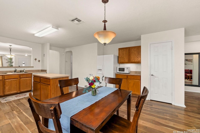 dining space featuring visible vents, arched walkways, baseboards, and wood finished floors