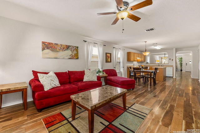 living area featuring a ceiling fan, dark wood-type flooring, arched walkways, and visible vents