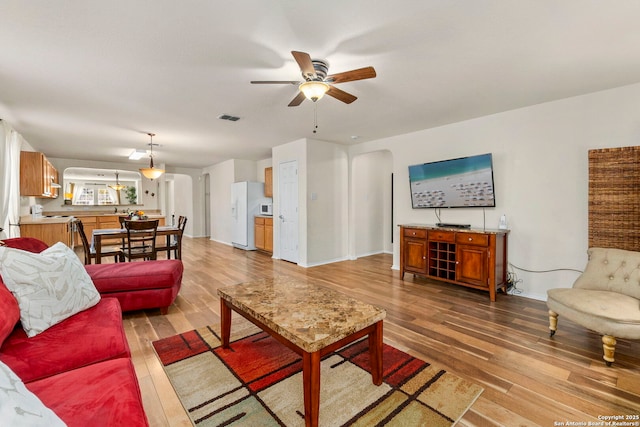 living area with visible vents, baseboards, light wood-style flooring, arched walkways, and a ceiling fan