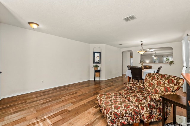 living area with visible vents, arched walkways, wood-type flooring, and a textured ceiling