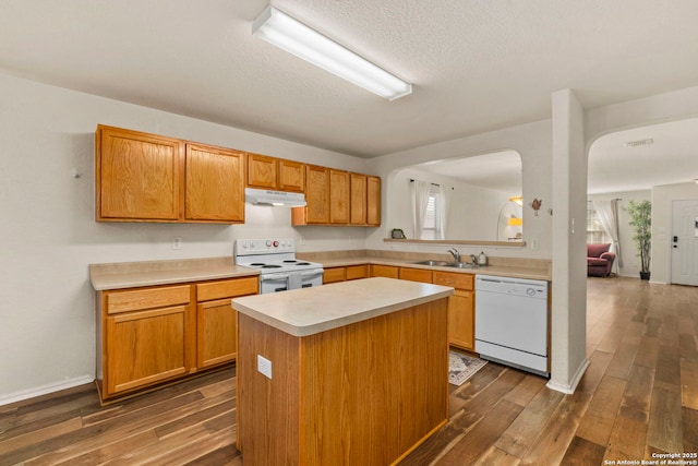 kitchen with under cabinet range hood, a kitchen island, dark wood finished floors, white appliances, and light countertops