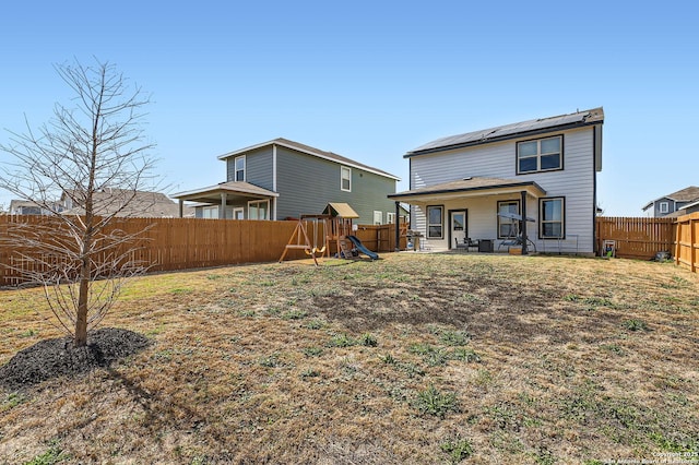 back of house with roof mounted solar panels, a playground, and a fenced backyard