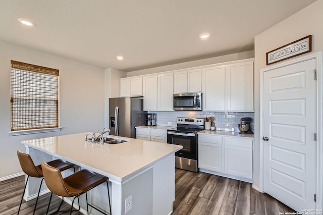 kitchen with backsplash, a center island with sink, white cabinets, stainless steel appliances, and a sink